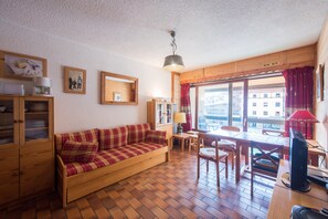 Una sala de estar acogedora con un sofá de madera, una mesa de comedor y sillas. Hay una ventana con cortinas, una lámpara y un ventilador de techo.