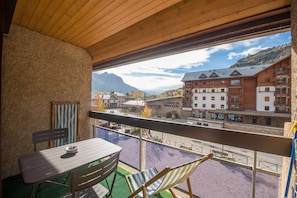 A balcony with a table and chairs, a view of a town with buildings and mountains, and a wooden ceiling. - Serre-Chevalier Vallée Briançon (Briançon)
