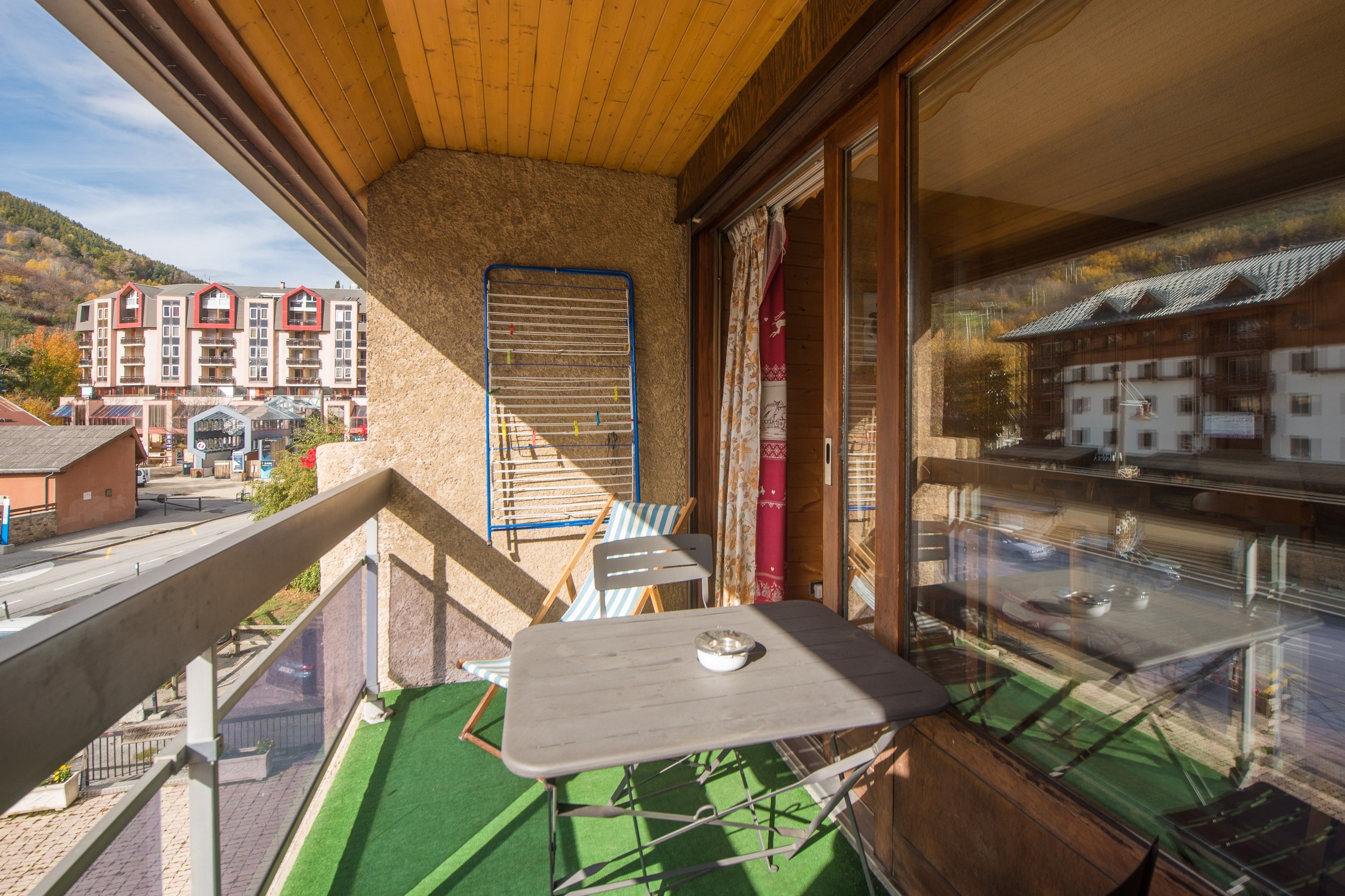 A balcony with a table and chairs, a drying rack, and a view of buildings in the background.
