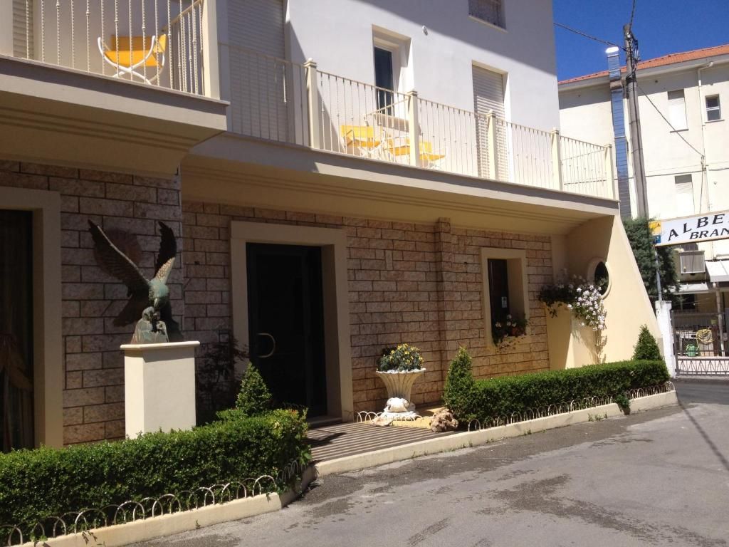 Un bâtiment à la façade en briques, un balcon avec des chaises jaunes, une statue et une enseigne indiquant « ALBERT BRANI ».