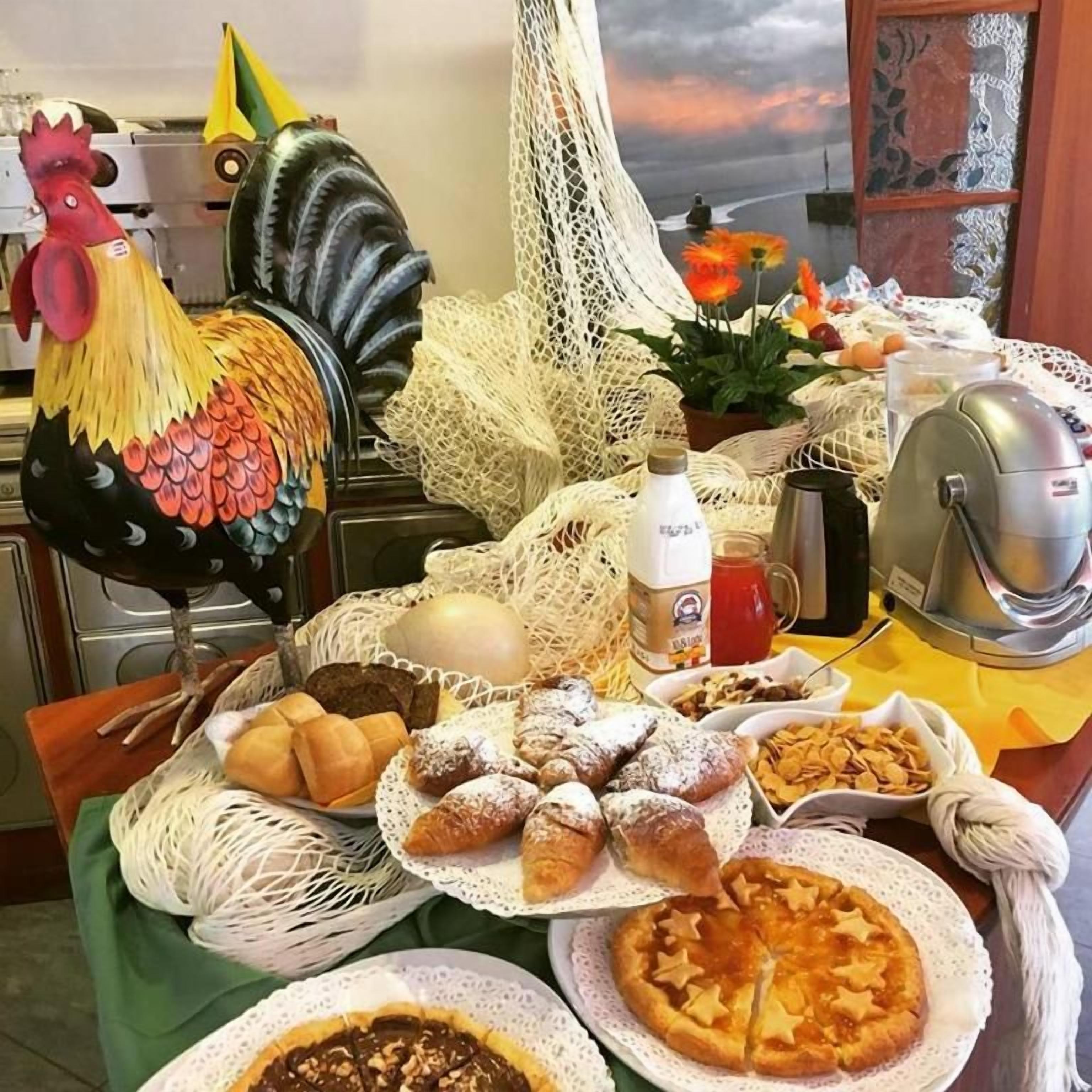 Ein reichhaltiges Frühstücksbuffet mit verschiedenen Backwaren, einer Dekoration mit einem Hahn und einem schönen Ausblick durch ein Fenster.