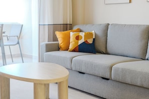A modern living room with a grey sofa, two cushions, a round wooden table, and a chair. - Blue Horizon apartment in Marina Palace (Adeje)