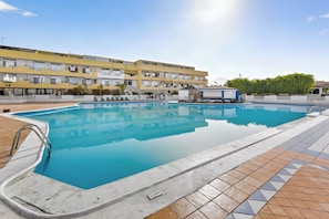 A swimming pool with a tiled deck, a building with balconies in the background, and a clear sky. - Blue Horizon apartment in Marina Palace (Adeje)