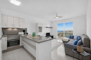 A modern kitchen with a central island, a dining area with a sofa, and a large window offering a city view. - Island Village Paradise apartment (Costa Adeje)