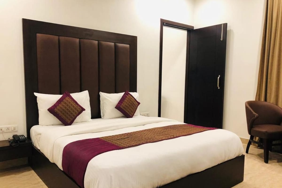 A hotel room with a large bed, a nightstand, a chair, and a wardrobe.