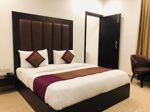 A hotel room with a large bed, a nightstand, a chair, and a wardrobe.