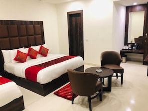 A hotel room with a large bed, two chairs, a small table, and a mirror.