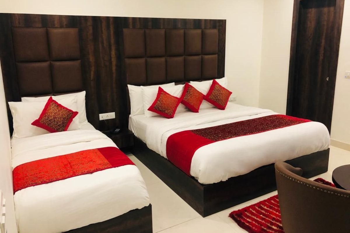 A hotel room with two beds, dark headboards, white bedding, and red accents.