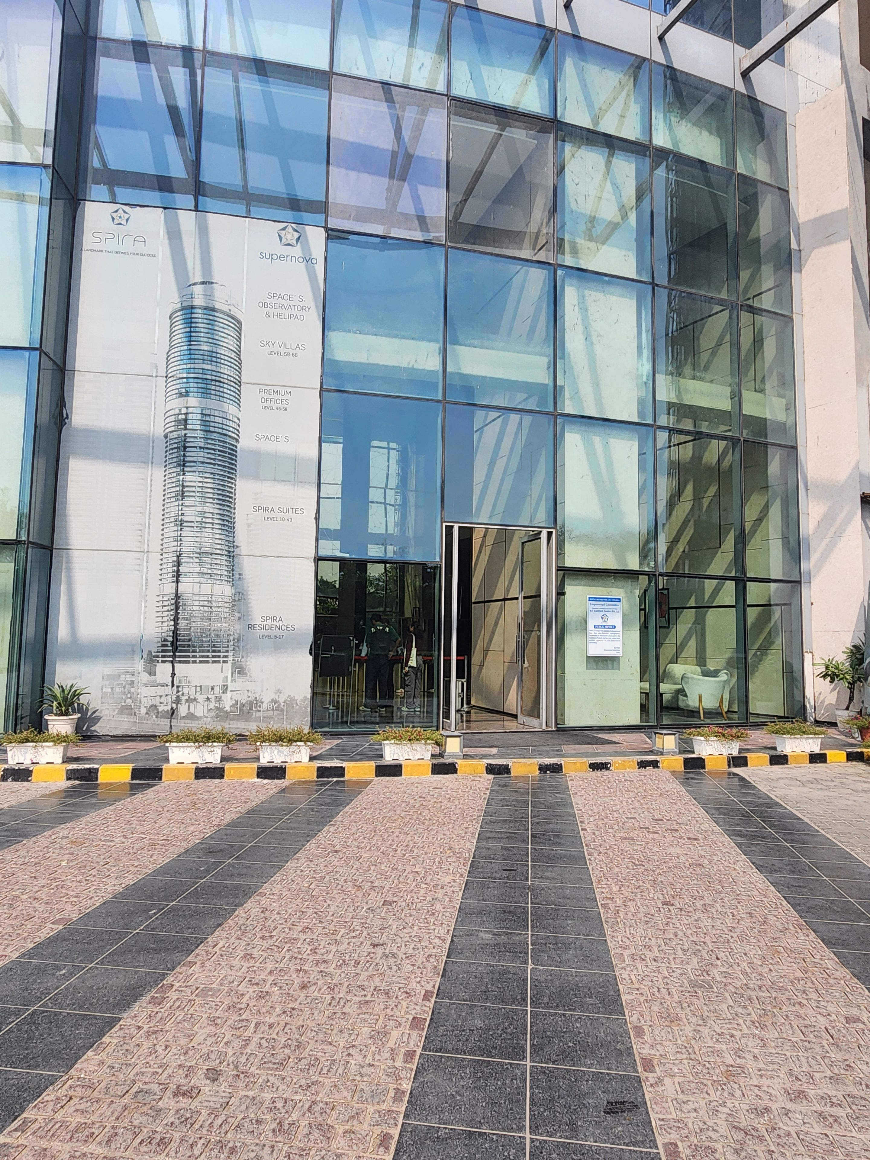 A modern building with a glass facade, a prominent entrance, and a landscaped area with potted plants.