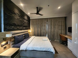 A modern hotel room with a large bed, a desk, a flat-screen TV, a ceiling fan, and a stone-textured accent wall. - Vinis Cloud Stay  (Delhi)