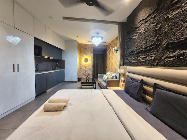 A modern hotel room with a large bed, a sitting area with a sofa, a small table, and a kitchen area with cabinets and a microwave. - Vinis Cloud Stay (New Delhi)