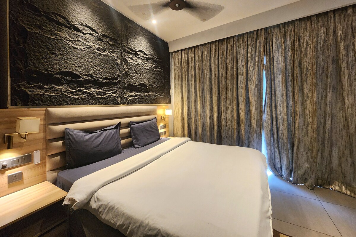 A modern bedroom with a large bed, a headboard with integrated lighting, a wall-mounted clock, and a ceiling fan.