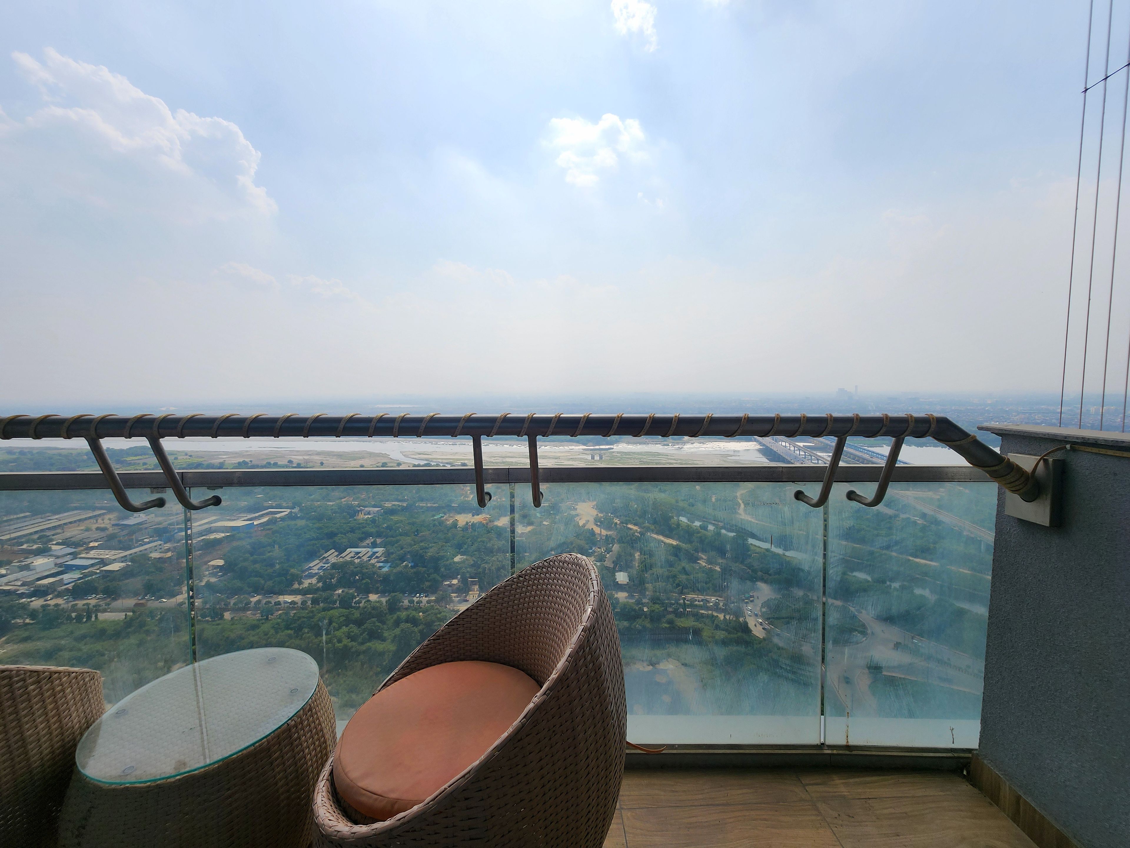 A balcony with wicker furniture and a glass barrier overlooking a landscape with fields and a river.