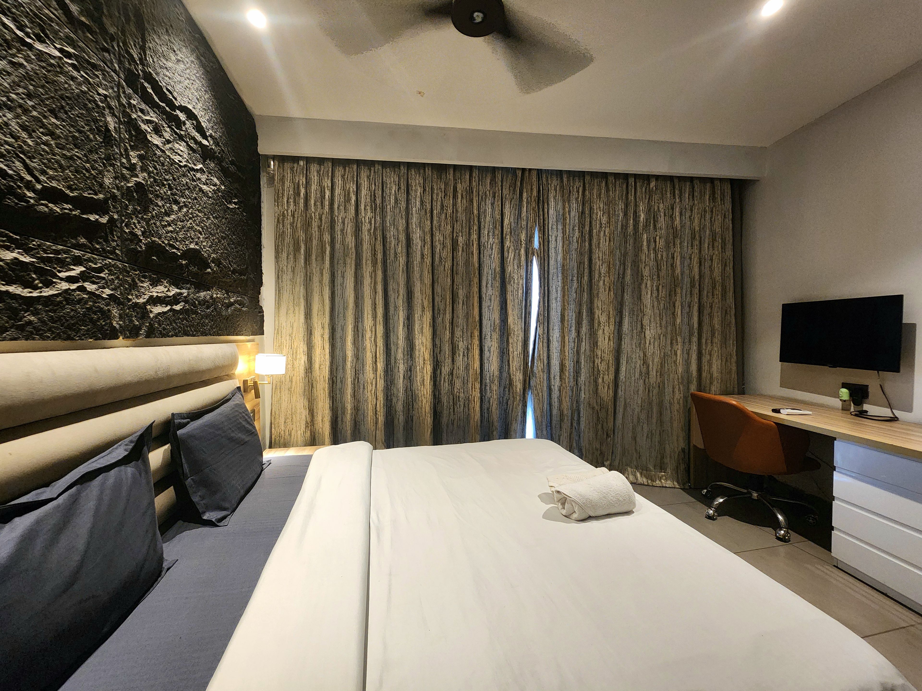 Una habitación de hotel con cama, escritorio, televisor y cortina.