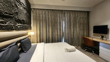 A hotel room with a bed, a desk, a television, and a curtain.