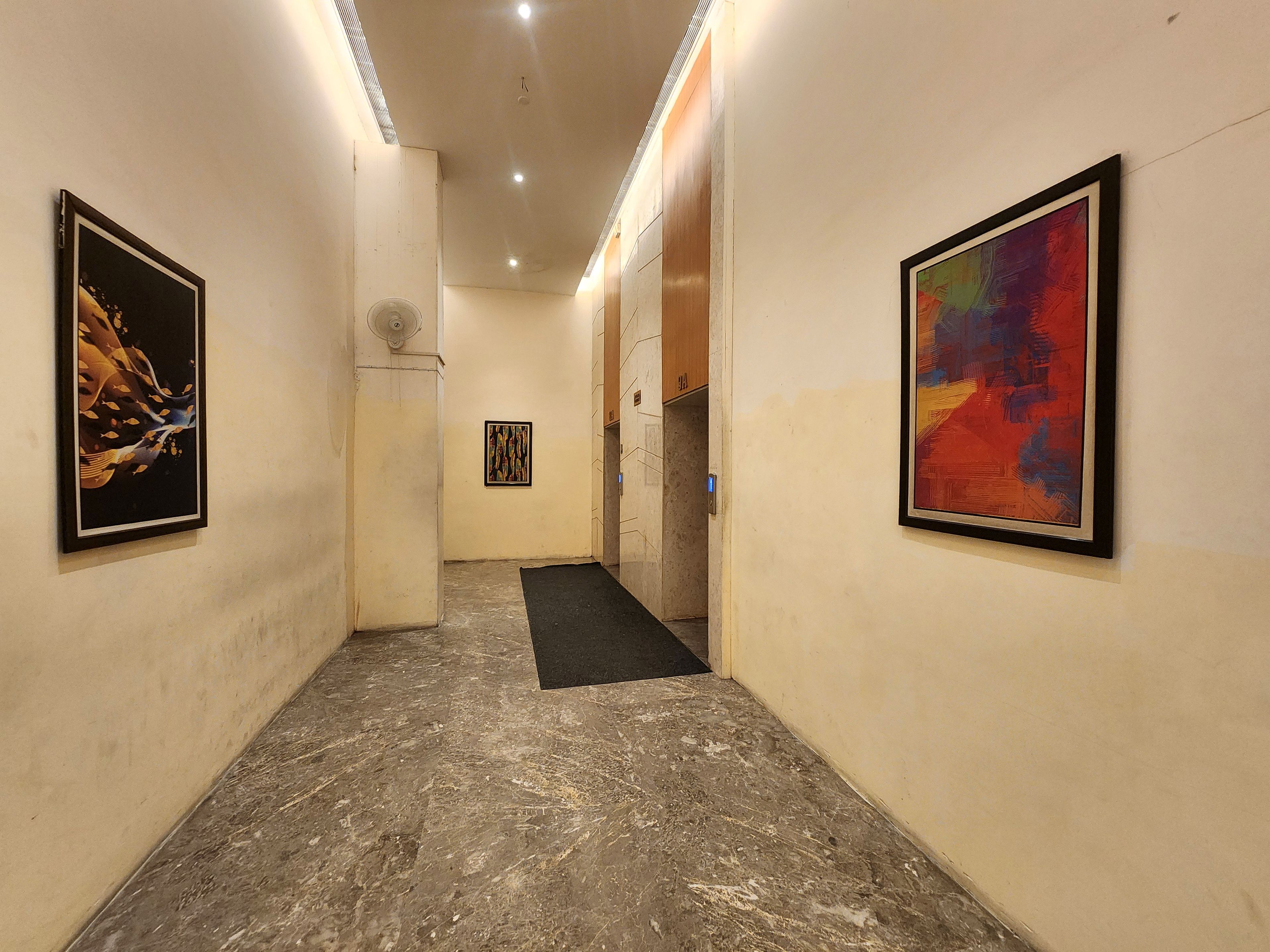 A hallway with artwork on the walls, a marble floor, and a black mat at the end.