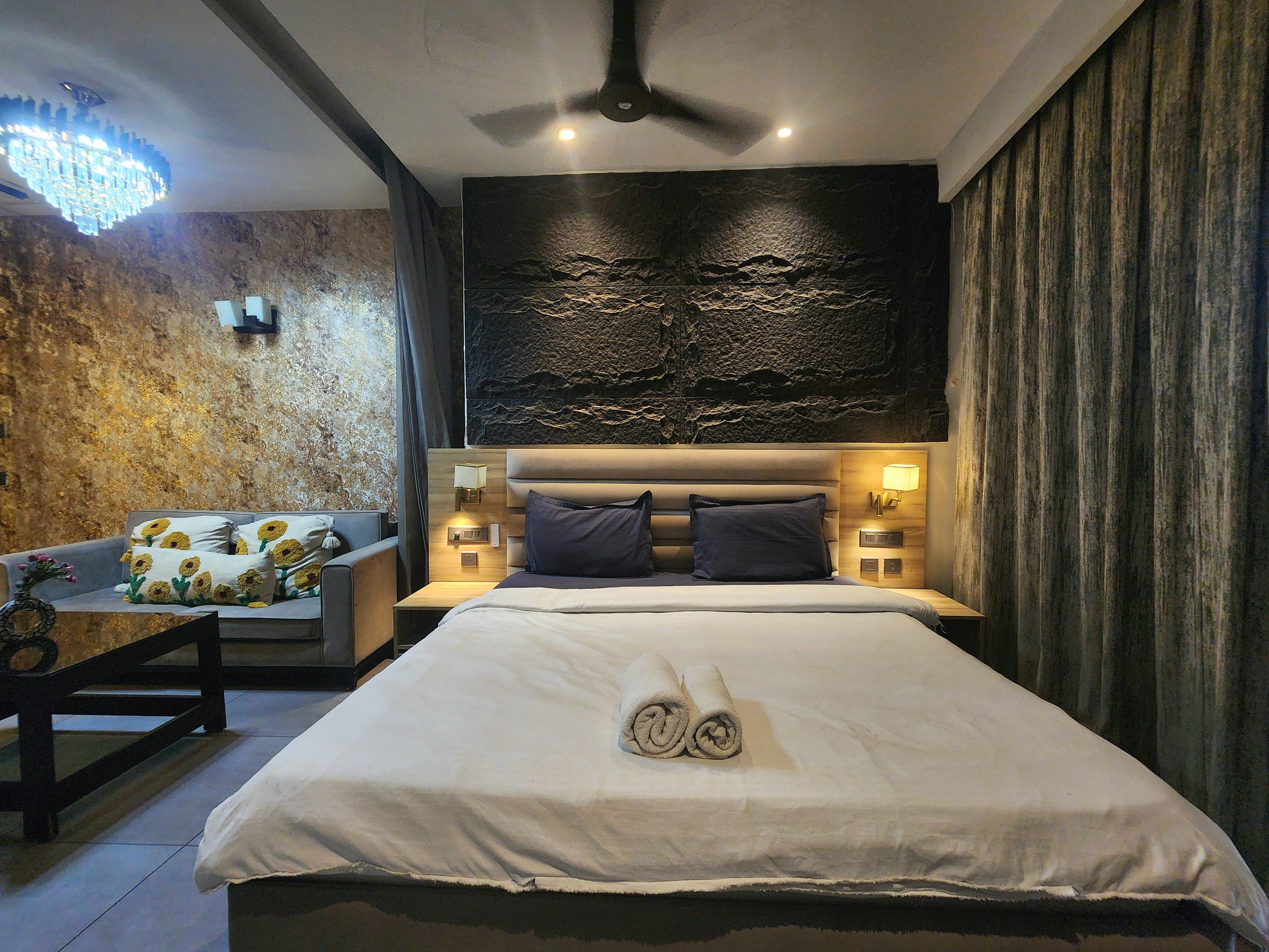 A modern hotel room with a large bed, a sofa, a ceiling fan, and a textured wall.