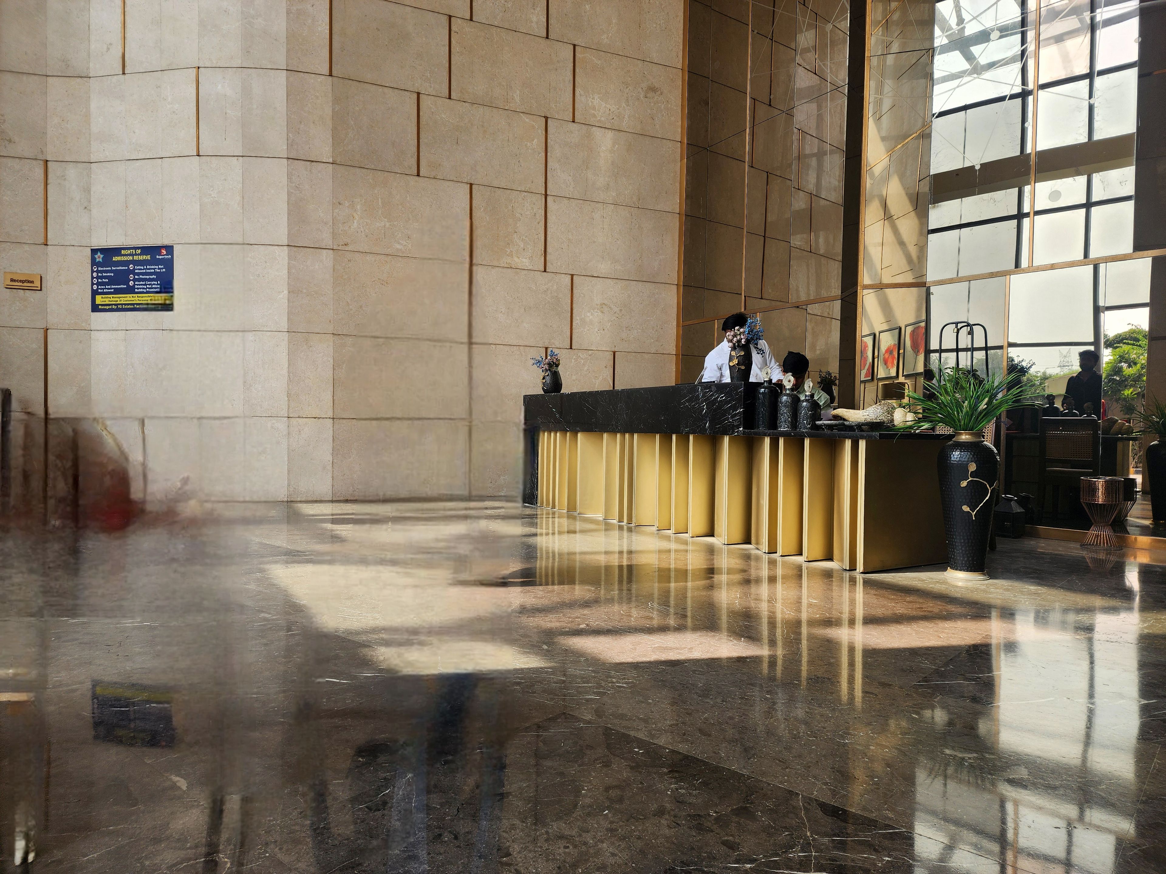 Zona de recepción de hotel con suelo de mármol, mostrador de recepción y un amplio ventanal.