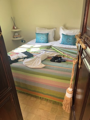 Una habitación de hotel con una cama, una mesita de noche con lámpara y un estante en la pared con caja de pañuelos.