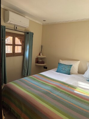 Une chambre avec un lit, une fenêtre avec des rideaux, un appareil de climatisation et une petite étagère sur laquelle se trouve une boîte de mouchoirs.