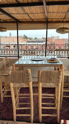 Eine Terrasse mit einem Glastisch, umgeben von Flehr-Stühlen, einem gemusterten Teppich und Blick auf Gebäude in der Ferne.
