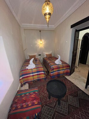 Ein Hotelzimmer mit zwei Betten, einem kleinen Tisch, einem gemusterten Teppich und einer dekorativen Hängeleuchte.