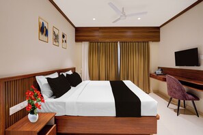 Ein Hotelzimmer mit Bett, Schreibtisch, Stuhl, Fernseher und Deckenventilator.