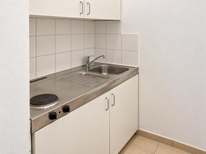 Eine kompakte Küche mit Spüle aus Edelstahl, einem Kochfeld und weißen Schränken.