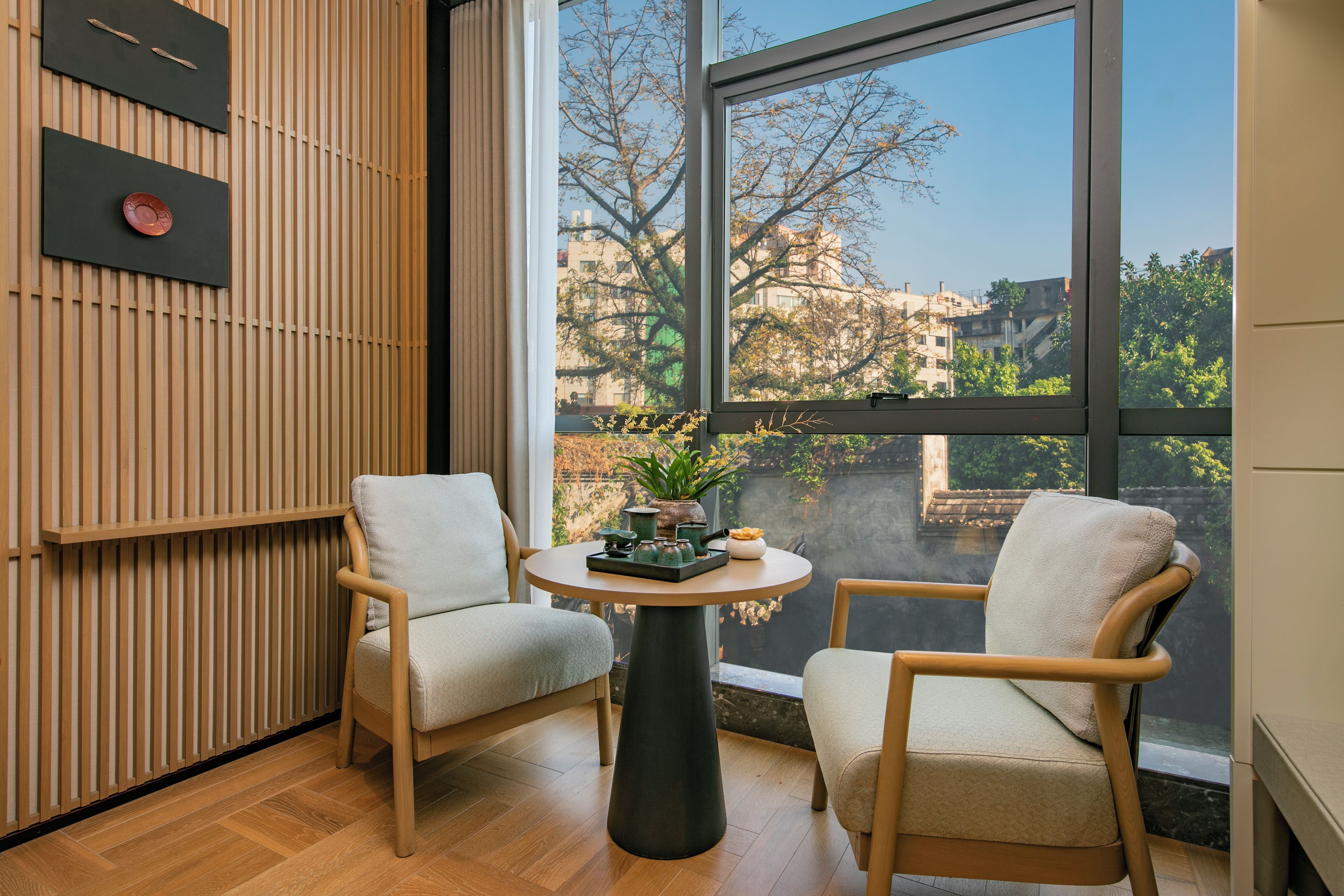 Una habitación moderna con dos sillas, una mesa redonda y un ventanal con vistas a edificios y árboles.