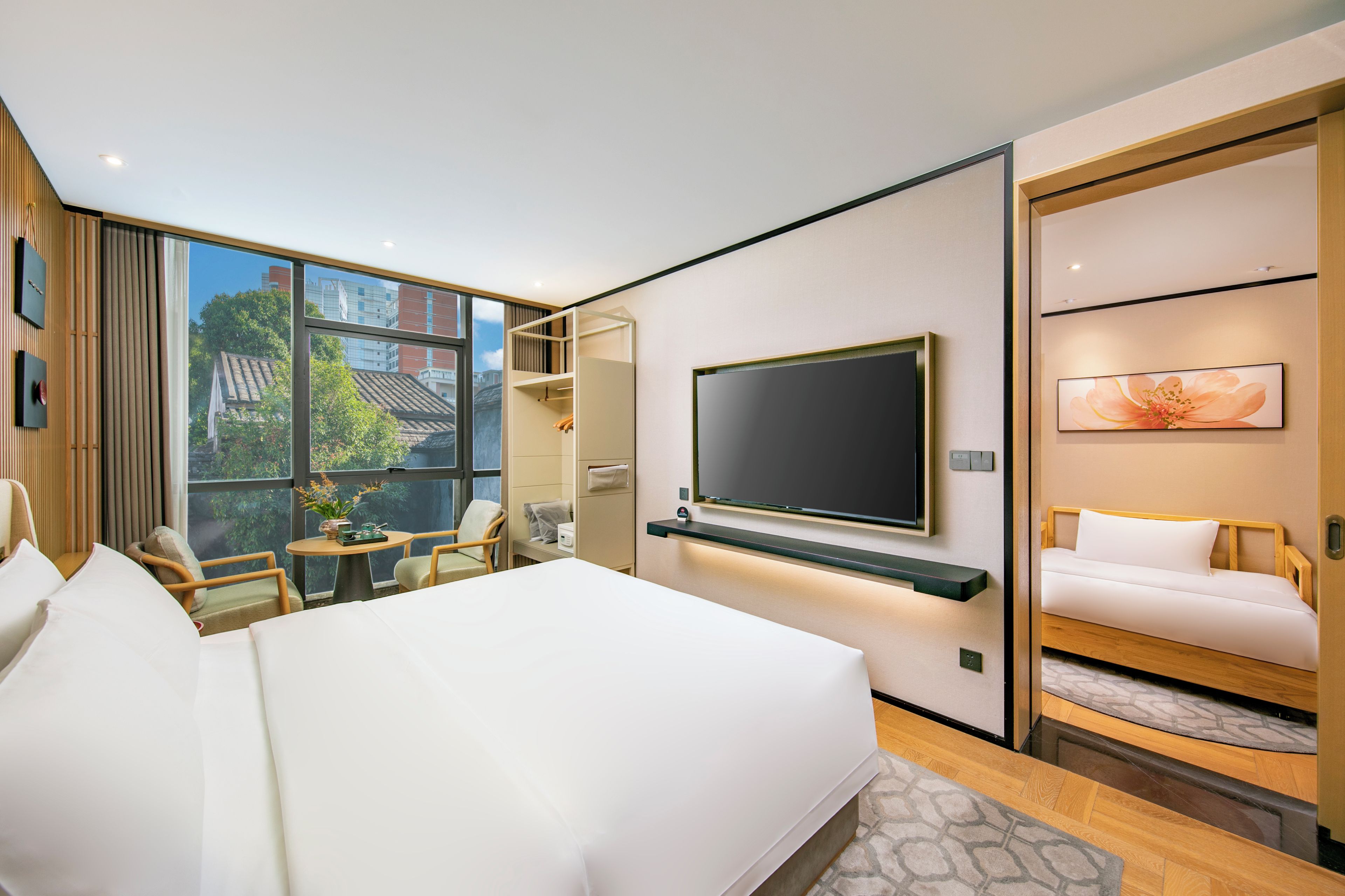 Habitación de hotel moderna con una cama grande, un televisor montado en la pared, una zona de estar con sillas y vistas al exterior.