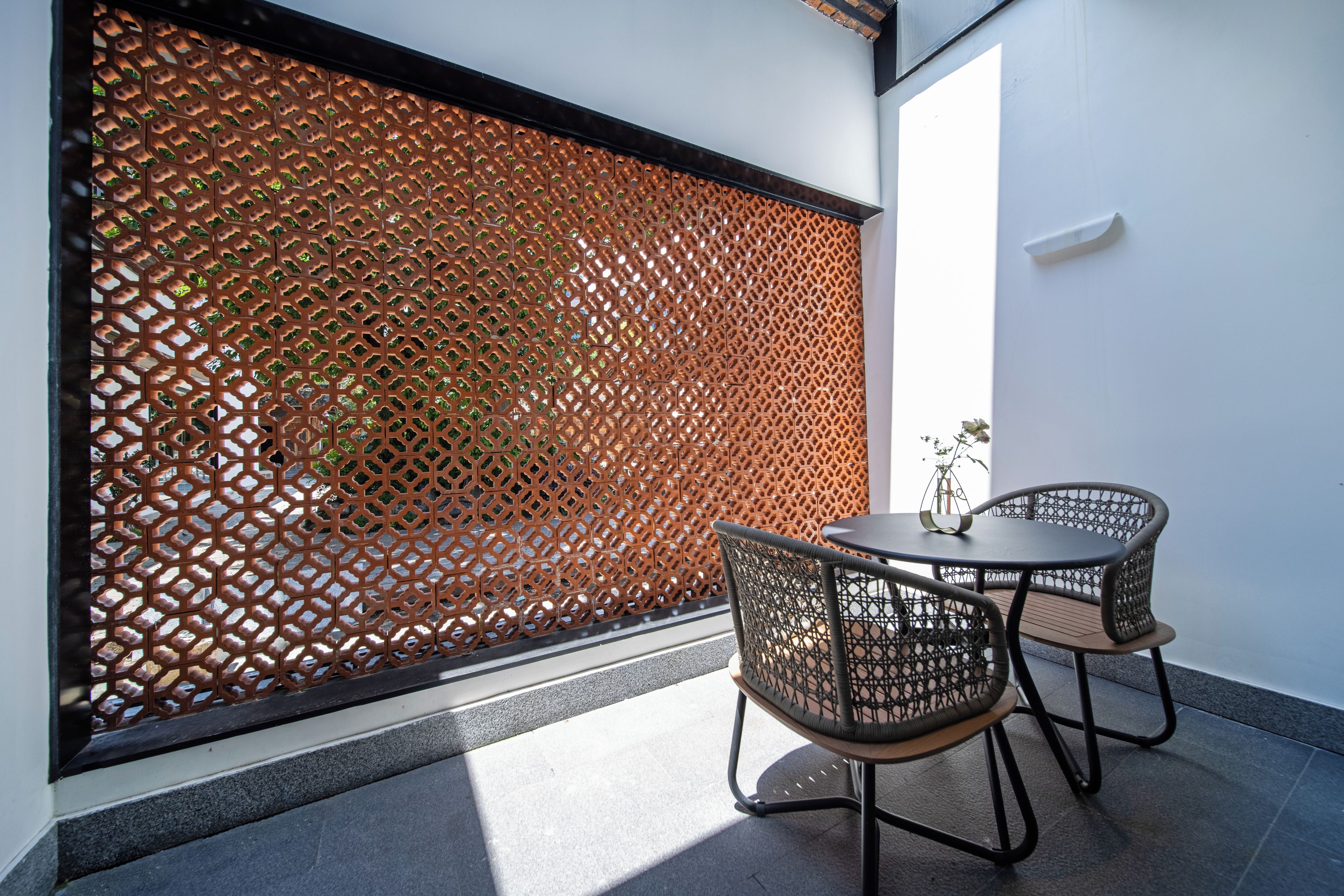 Une pièce avec un paravent à motifs, deux fauteuils en osier et une petite table.