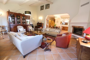 A spacious living room with a fireplace, a dining area, and a kitchen visible through an archway. - Air-co villa, Luberon views, heated pool, sleeps 8 (La Motte-d´Aigues)