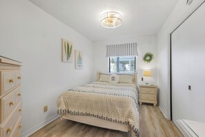 A bedroom with a bed, nightstand, dresser, and a window with blinds. - Gulf Shores Cozy Getaway: 1BR Condo Pool Access/5 Minute Walk to Beach (Gulf Shores)