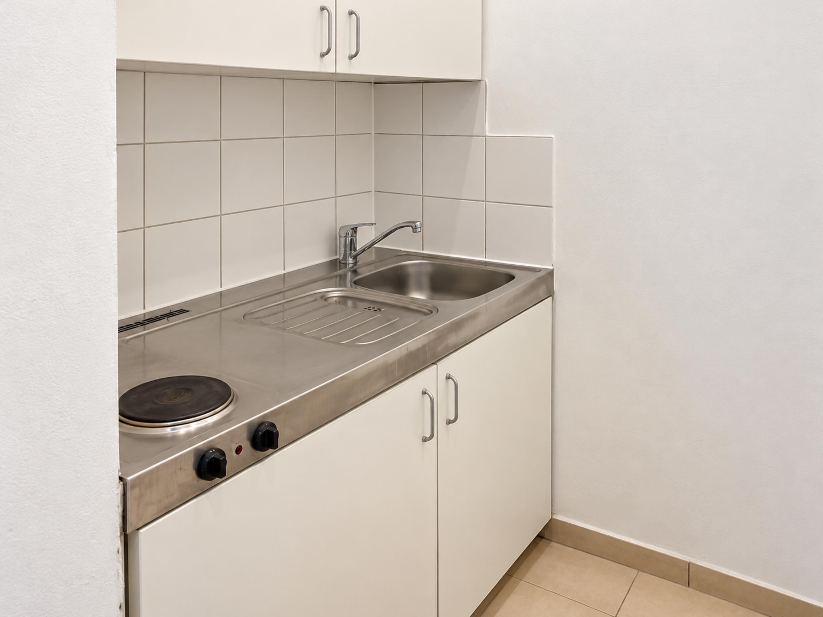 A compact kitchen with a stainless steel sink, a stovetop, and white cabinets.