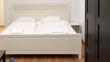 A bed with white bedding and a wooden headboard, a nightstand with a lamp, and a dark door.