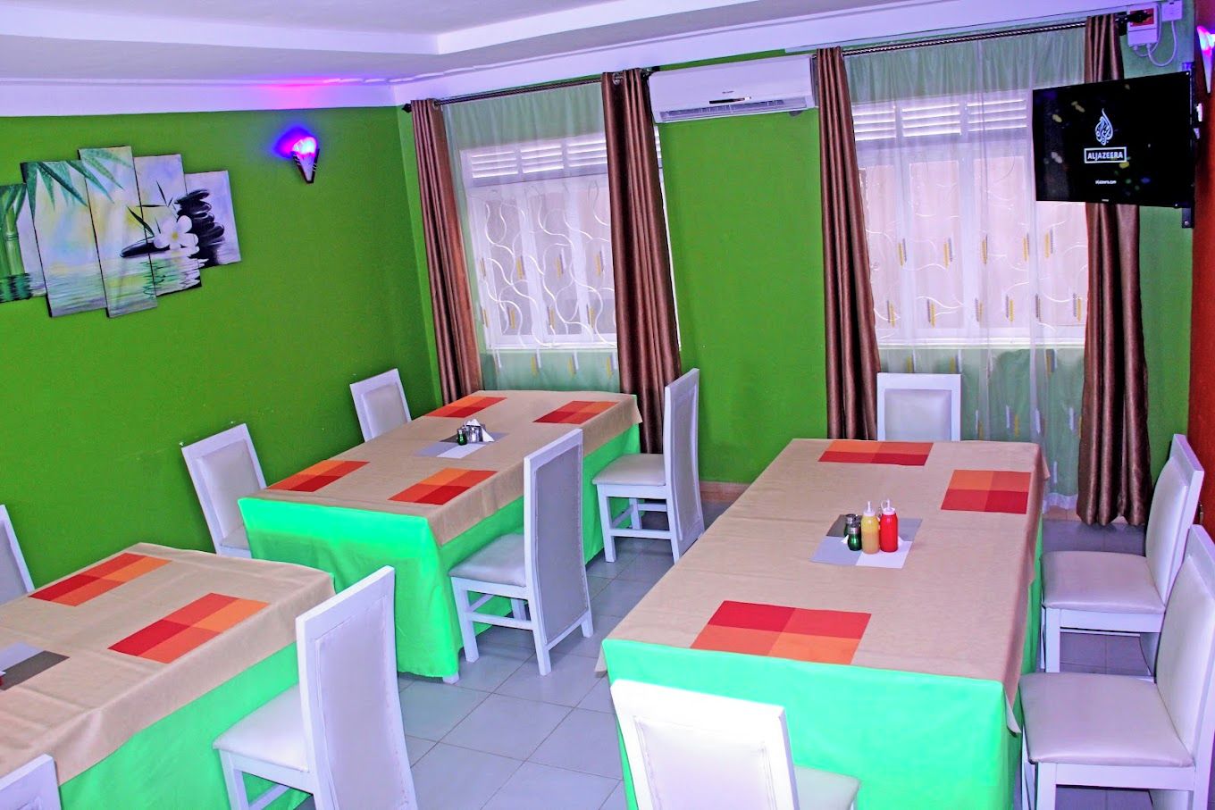Un salón de conferencias con paredes verdes, sillas blancas y mesas con manteles de colores.