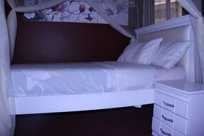 A single bed with a canopy, a bedside table with drawers, and a floral wall design.