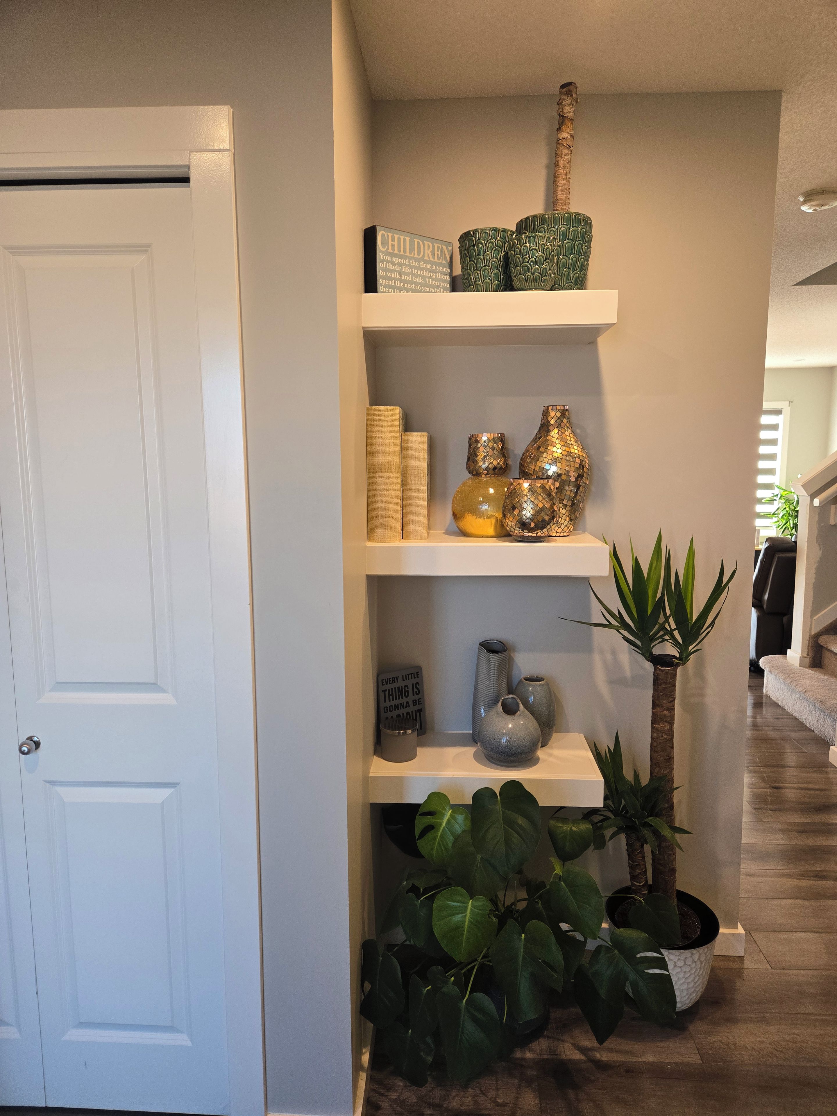 Een gang met een witte deur, een plank met decoratieve spullen en een potplant.