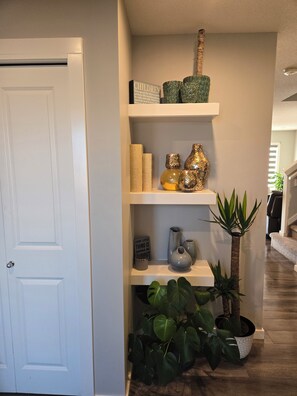 Un passadís amb una porta blanca, una prestatgeria amb objectes decoratius i una planta en test.