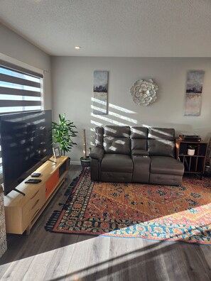 A living room with a sofa, a TV, a plant, and a patterned rug. - Modern home w/ Full Kitchen & In-Unit Laundry (Edmonton)