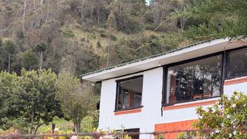 Una casa moderna amb façana blanca i detalls vermells, envoltada de vegetació abundant i plantes amb flors.