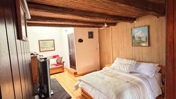 Habitació amb sostre de fusta, llit amb roba de llit blanca, televisió sobre un suport i un quadre a la paret.
