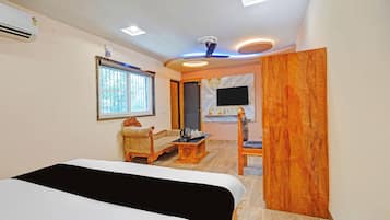 A hotel room with a bed, a sofa, a wooden chair, a television mounted on the wall, and a ceiling fan.
