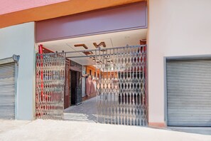 A hotel entrance with a metal gate, a staircase leading to the interior, and a closed shutter on the right.