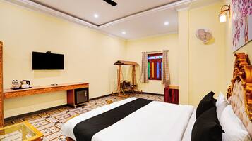 Habitación de hotel con cama, escritorio, televisor, ventilador de techo y ventana con cortinas.