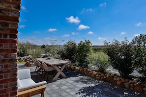 An outdoor patio with a wooden table and chairs, surrounded by a stone wall and greenery. - Stylish living with a view of the salt marshes, including a sauna, fireplace, and terrace (Sylt)