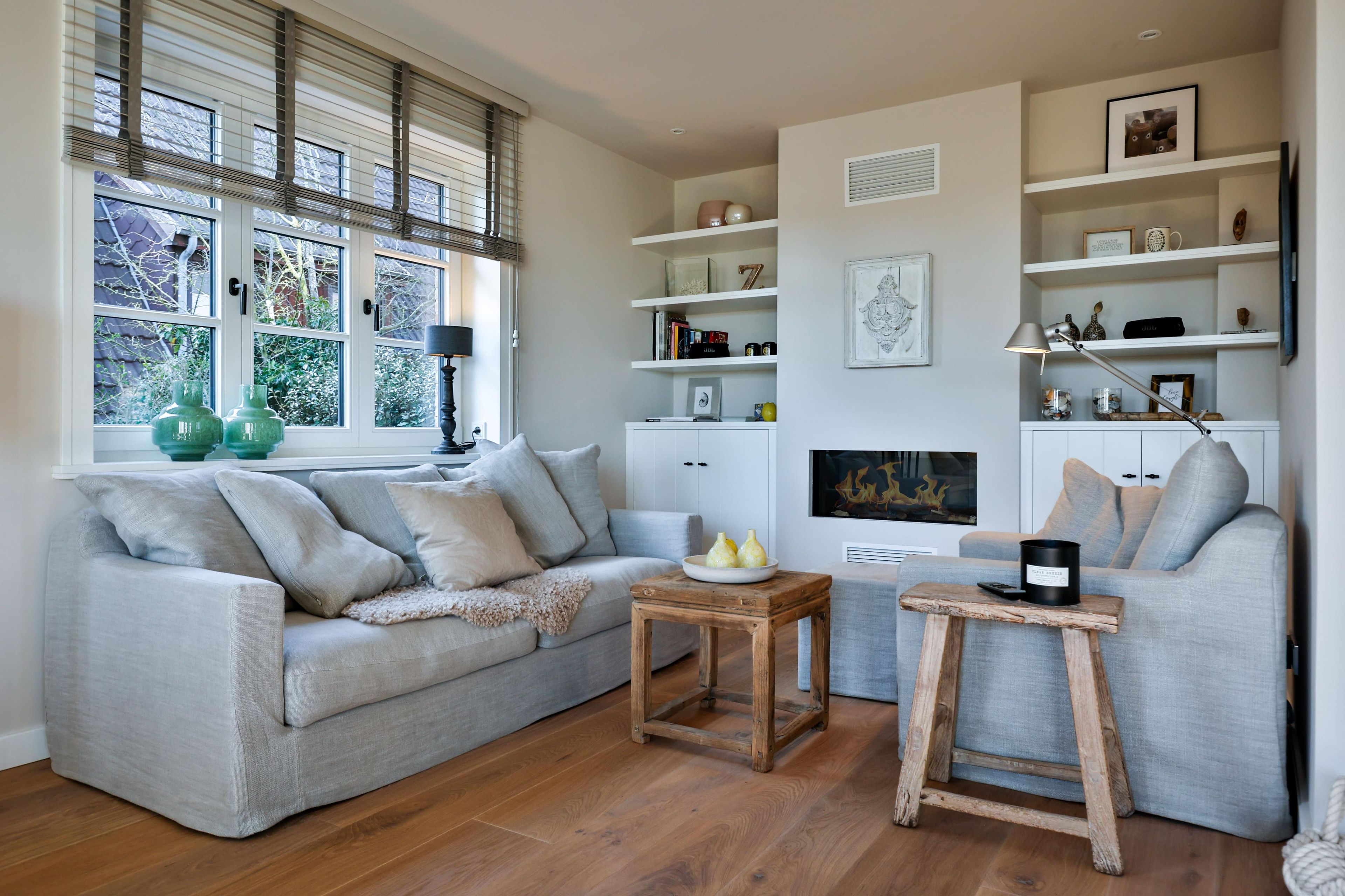 A living room with a grey sofa, a wooden coffee table, and a fireplace. There are shelves with decorative items and a television mounted on the wall.