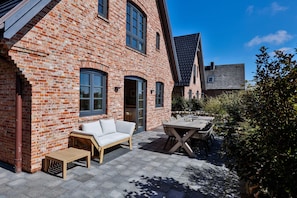 A brick house with a patio, a sofa, and a table. - Stylish living with a view of the salt marshes, including a sauna, fireplace, and terrace (Sylt)