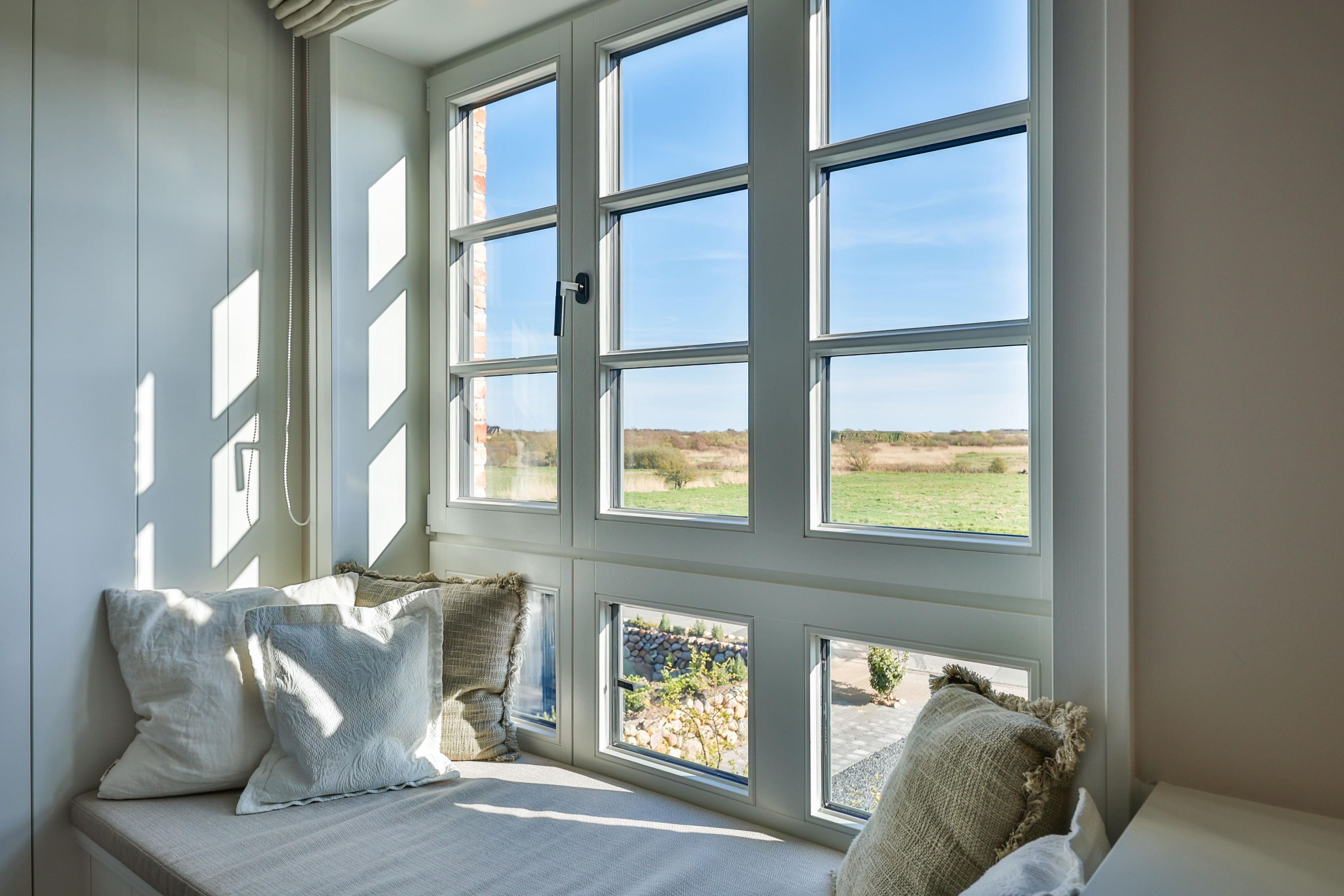 A room with a large window, a bench with cushions, and a view of a grassy field.