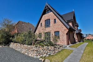 A brick house with a steep gable roof, a stone wall, and a gravel driveway. - Stylish living with a view of the salt marshes, including a sauna, fireplace, and terrace (Sylt)